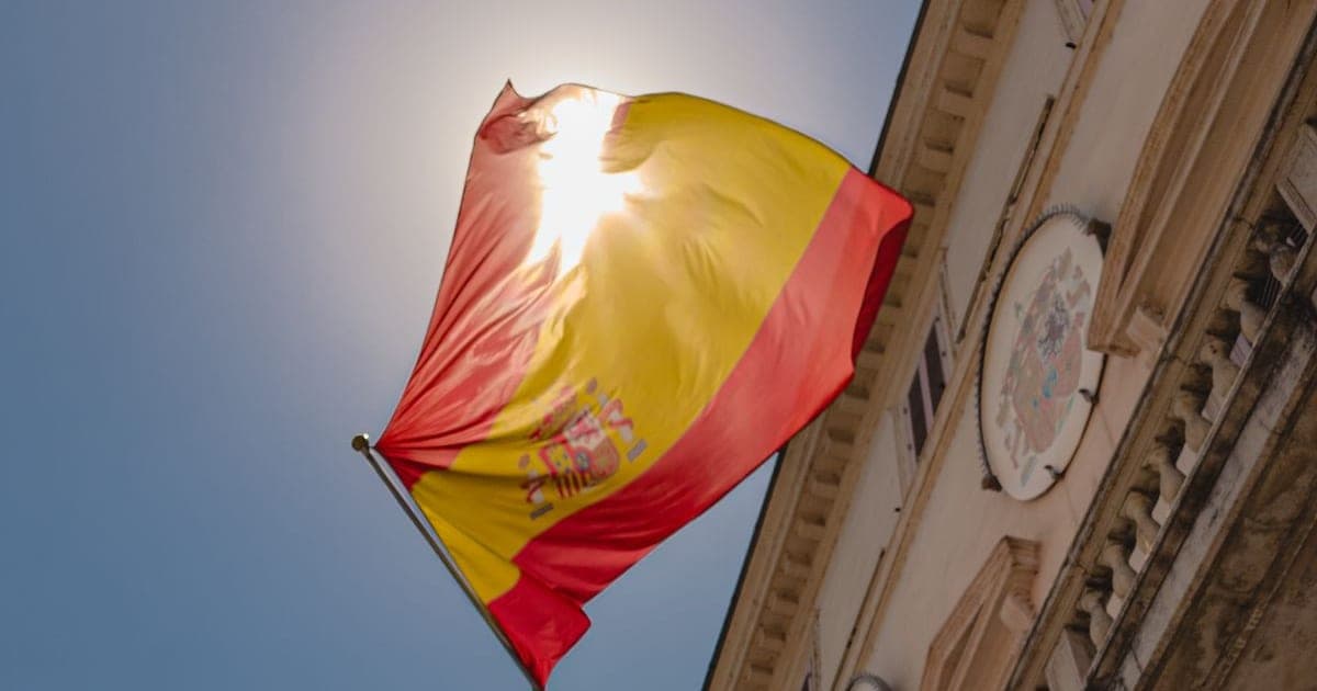 Bandera española flameando a contraluz junto a la fachada de un edificio histórico